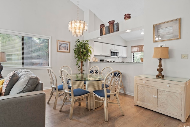 dining space with light hardwood / wood-style floors, high vaulted ceiling, and an inviting chandelier