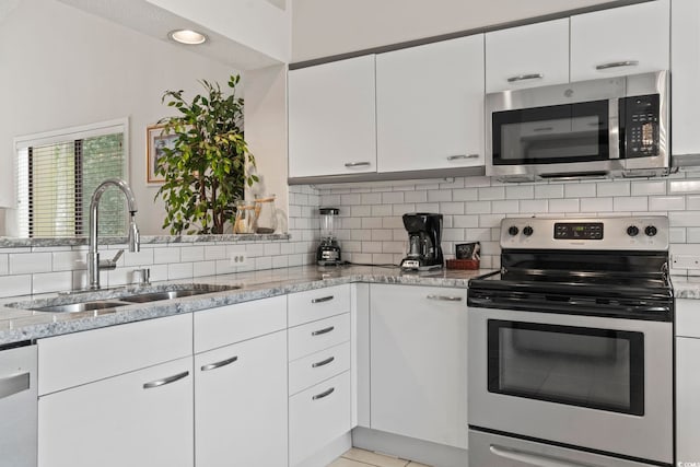 kitchen featuring light stone countertops, sink, backsplash, white cabinets, and appliances with stainless steel finishes