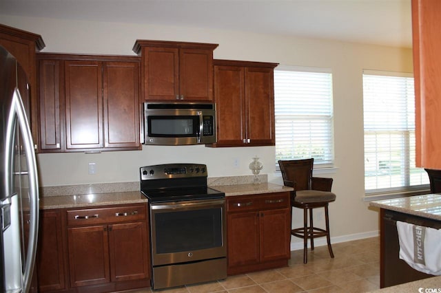 kitchen with light stone countertops, light tile patterned floors, and stainless steel appliances