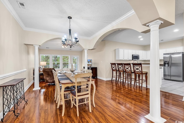 dining area with an inviting chandelier, decorative columns, dark hardwood / wood-style floors, and a textured ceiling