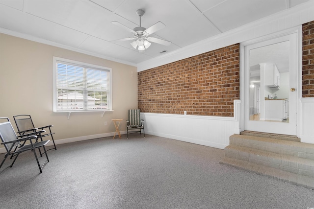 unfurnished room with carpet, ornamental molding, ceiling fan, and brick wall