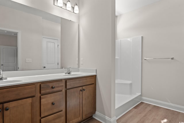 bathroom with double vanity, wood finished floors, a sink, and baseboards