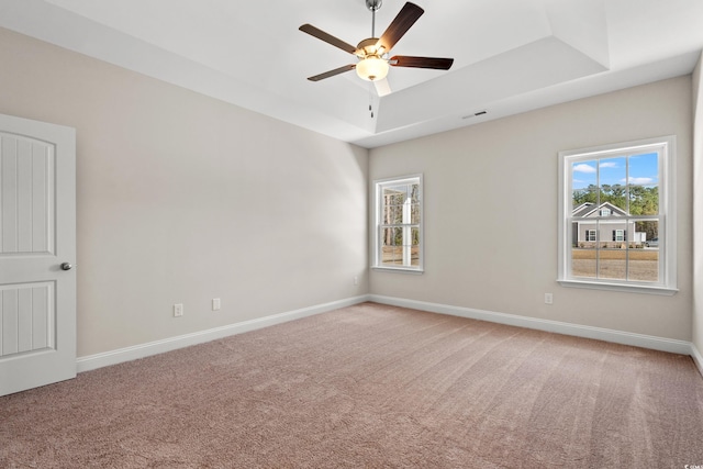 empty room featuring light carpet, visible vents, baseboards, and a raised ceiling