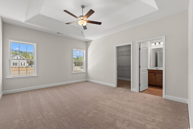 unfurnished bedroom with baseboards, a spacious closet, a tray ceiling, and light colored carpet