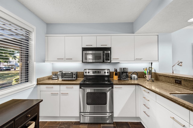 kitchen with white cabinets, dark stone counters, a textured ceiling, and appliances with stainless steel finishes