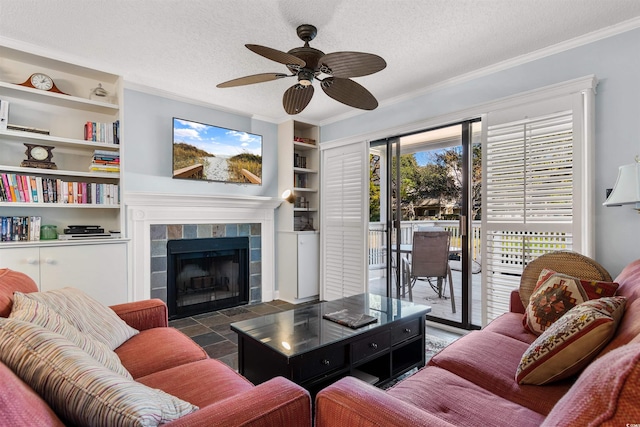 living room with a tiled fireplace, ceiling fan, built in features, and a textured ceiling