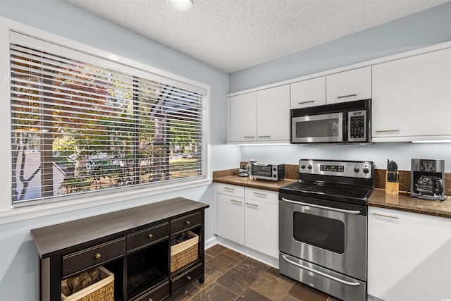 kitchen featuring white cabinets, a textured ceiling, appliances with stainless steel finishes, and dark stone counters