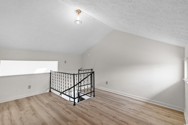 bonus room featuring a textured ceiling, light wood-type flooring, and lofted ceiling with skylight