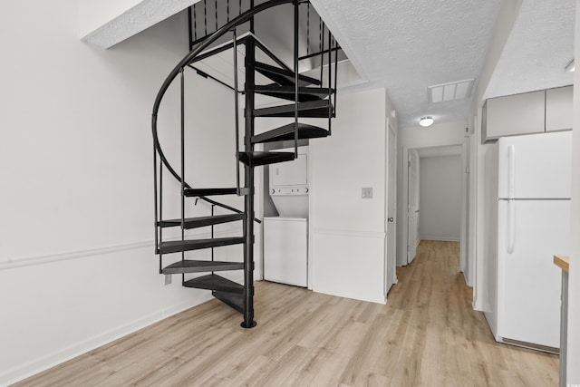 stairs featuring a textured ceiling, hardwood / wood-style floors, and stacked washer / drying machine