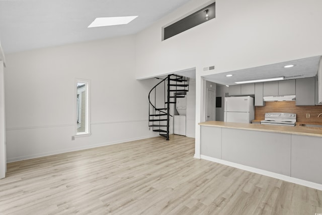 unfurnished living room with high vaulted ceiling, a skylight, sink, and light hardwood / wood-style floors