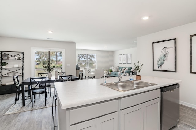 kitchen featuring white cabinets, sink, dishwasher, light hardwood / wood-style floors, and an island with sink