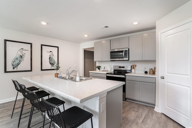 kitchen featuring gray cabinetry, sink, stainless steel appliances, and a kitchen island with sink