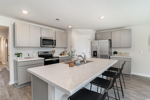 kitchen with gray cabinetry, sink, a center island with sink, and appliances with stainless steel finishes