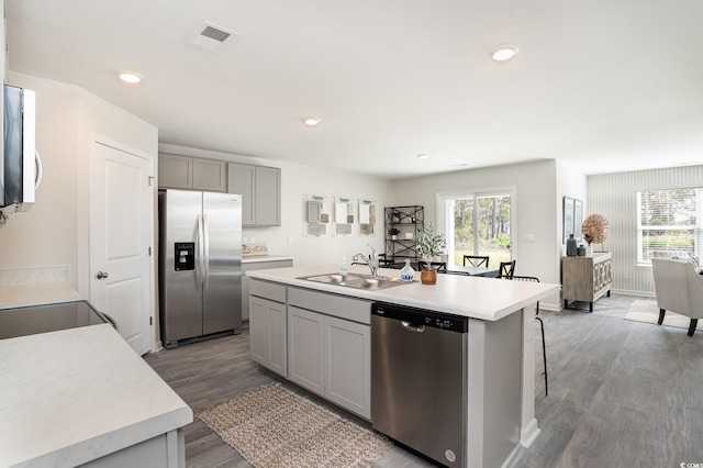 kitchen with gray cabinetry, sink, stainless steel appliances, a kitchen island with sink, and hardwood / wood-style flooring