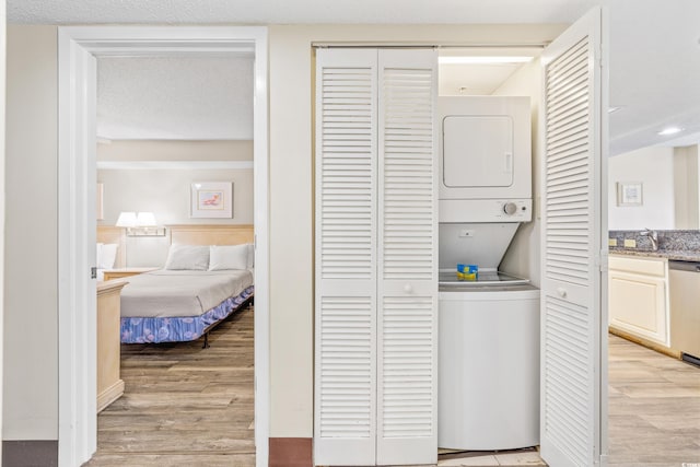 clothes washing area featuring light wood-type flooring, stacked washer and clothes dryer, a textured ceiling, and sink