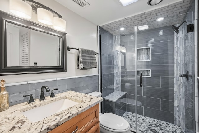 bathroom with vanity, backsplash, tile walls, toilet, and a shower with door