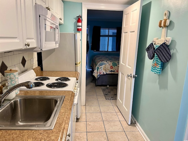 kitchen with white appliances, sink, light tile patterned floors, and white cabinets