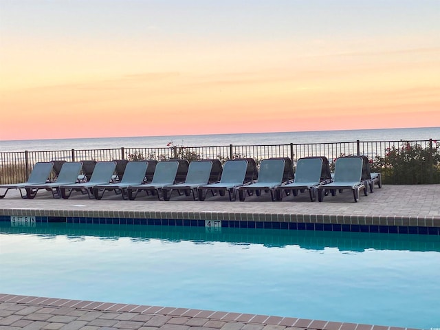 pool at dusk with a patio and a water view