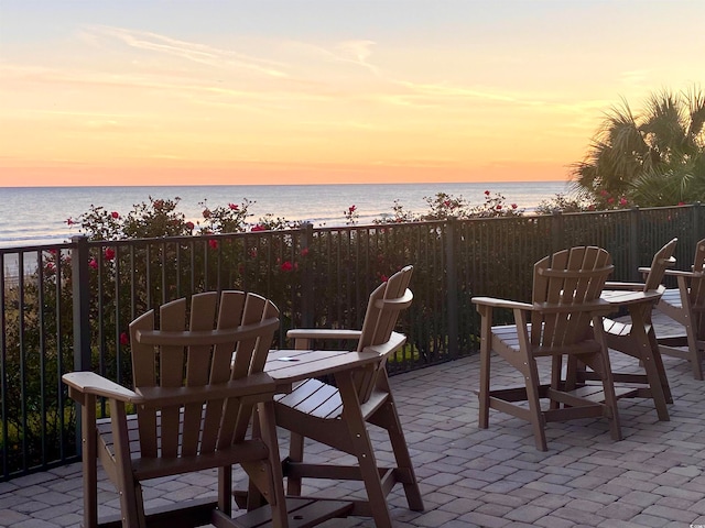 patio terrace at dusk with a water view and a view of the beach