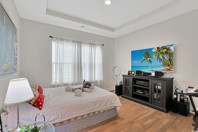 bedroom with multiple windows, a raised ceiling, and hardwood / wood-style floors