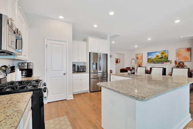 kitchen with appliances with stainless steel finishes, a kitchen island with sink, light hardwood / wood-style flooring, and white cabinetry