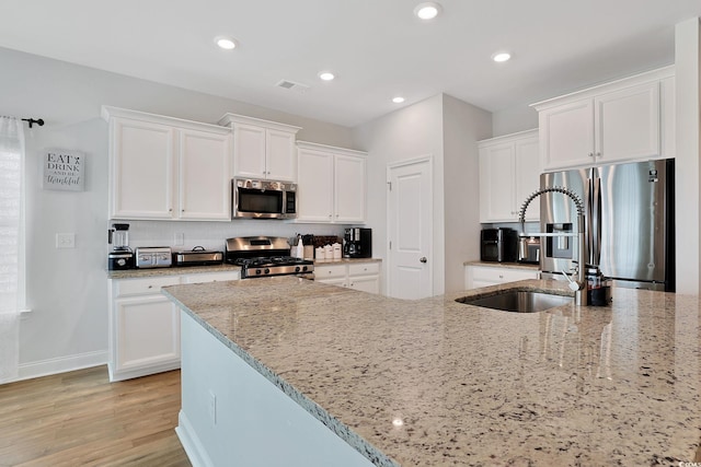 kitchen featuring light stone countertops, appliances with stainless steel finishes, light wood-type flooring, and white cabinetry