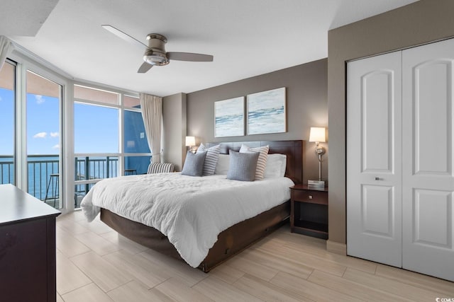 bedroom featuring access to outside, a water view, ceiling fan, and a closet