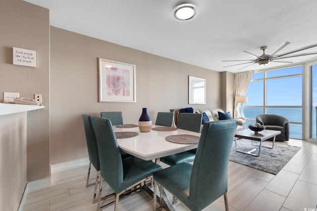 dining space featuring floor to ceiling windows, a water view, ceiling fan, and light hardwood / wood-style floors