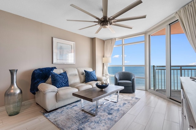 living room featuring ceiling fan, light wood-type flooring, floor to ceiling windows, and a water view