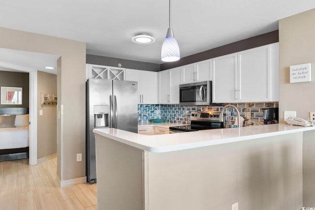 kitchen featuring white cabinets, hanging light fixtures, kitchen peninsula, stainless steel appliances, and decorative backsplash