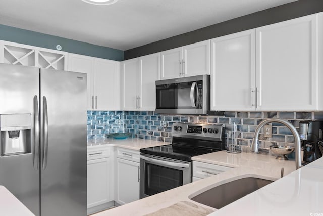 kitchen featuring decorative backsplash, white cabinetry, light stone countertops, stainless steel appliances, and sink