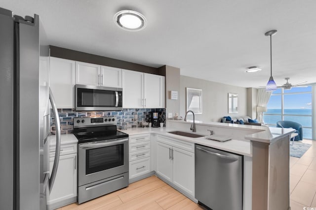 kitchen featuring appliances with stainless steel finishes, a water view, white cabinets, kitchen peninsula, and sink