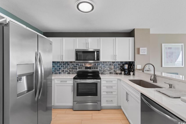 kitchen with light stone counters, white cabinets, sink, light hardwood / wood-style flooring, and appliances with stainless steel finishes