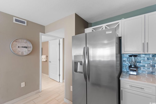 kitchen featuring stainless steel fridge, white cabinetry, backsplash, light wood-type flooring, and a textured ceiling