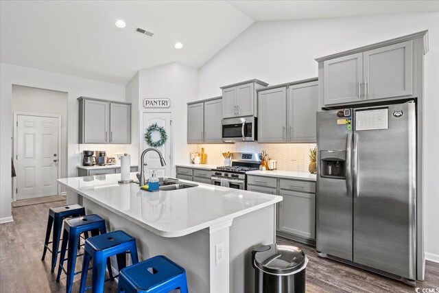 kitchen with a center island with sink, stainless steel appliances, a breakfast bar area, dark hardwood / wood-style flooring, and decorative backsplash