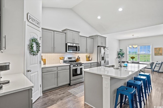 kitchen with a sink, a breakfast bar area, wood finished floors, gray cabinetry, and stainless steel appliances