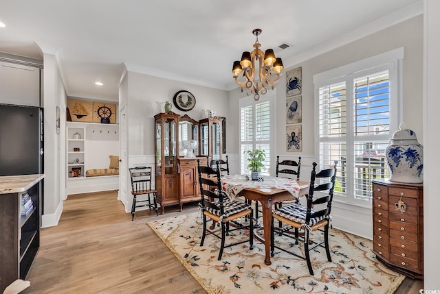 dining space featuring light wood-type flooring, ornamental molding, and a chandelier