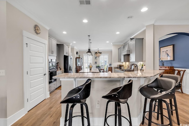 kitchen with gray cabinetry, decorative light fixtures, appliances with stainless steel finishes, a breakfast bar area, and light wood-type flooring