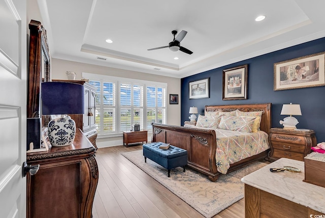 bedroom with ceiling fan, a tray ceiling, and wood-type flooring