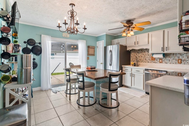 kitchen featuring light tile patterned flooring, decorative light fixtures, white cabinetry, stainless steel appliances, and ceiling fan with notable chandelier