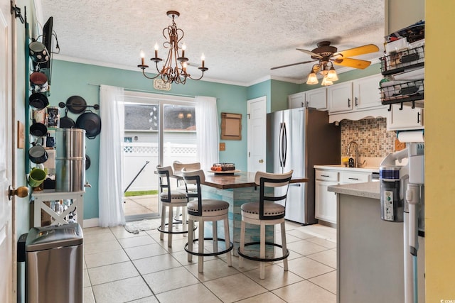 kitchen with light tile patterned flooring, ceiling fan with notable chandelier, white cabinets, stainless steel refrigerator, and decorative light fixtures