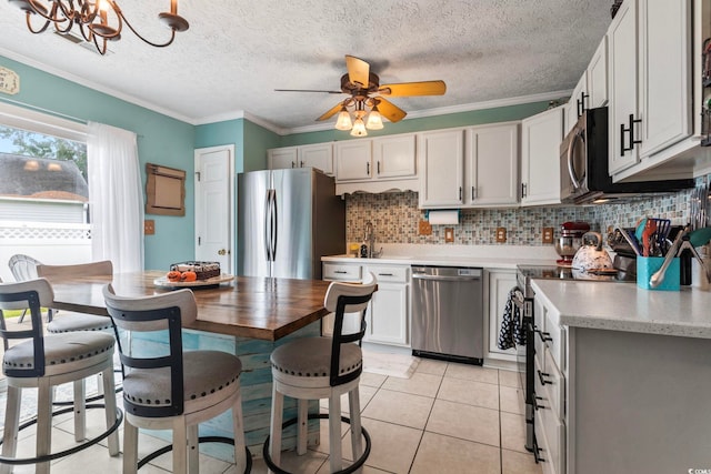 kitchen with appliances with stainless steel finishes, ceiling fan with notable chandelier, ornamental molding, and white cabinets