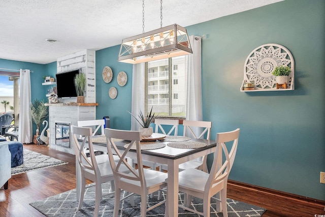 dining space featuring a textured ceiling, a stone fireplace, dark wood-type flooring, and a chandelier