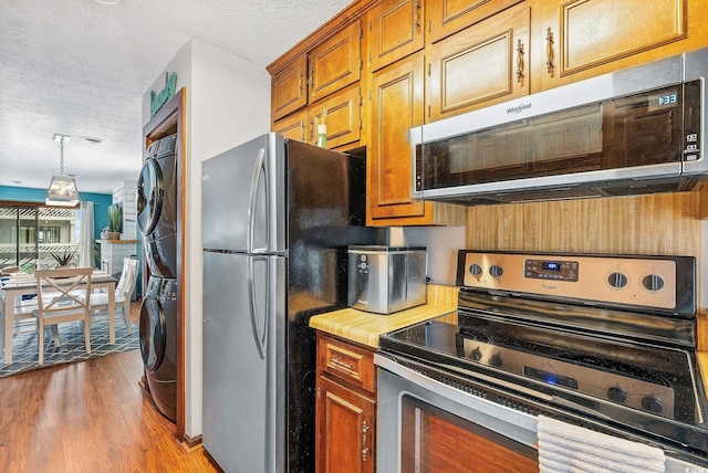 kitchen with light wood-type flooring, a textured ceiling, stainless steel appliances, decorative light fixtures, and stacked washer and clothes dryer