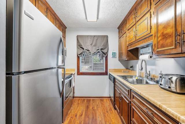 kitchen with a textured ceiling, light hardwood / wood-style floors, sink, and stainless steel appliances