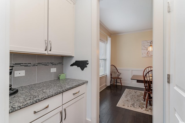 interior space featuring dark wood-style floors, light stone counters, wainscoting, tasteful backsplash, and white cabinetry