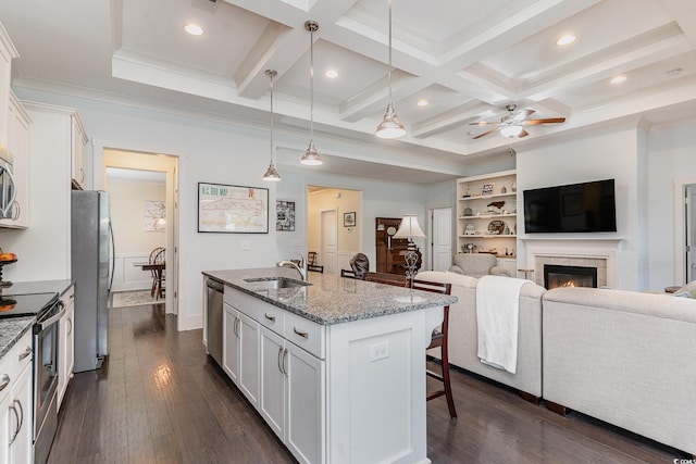 kitchen with pendant lighting, an island with sink, white cabinetry, a tiled fireplace, and stainless steel appliances