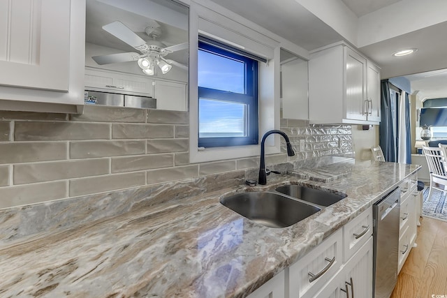 kitchen with dishwasher, light stone counters, sink, white cabinetry, and ceiling fan