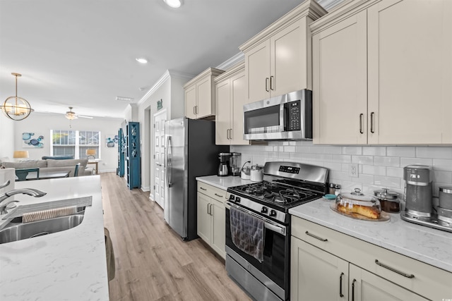 kitchen with light wood-type flooring, sink, appliances with stainless steel finishes, ornamental molding, and cream cabinets