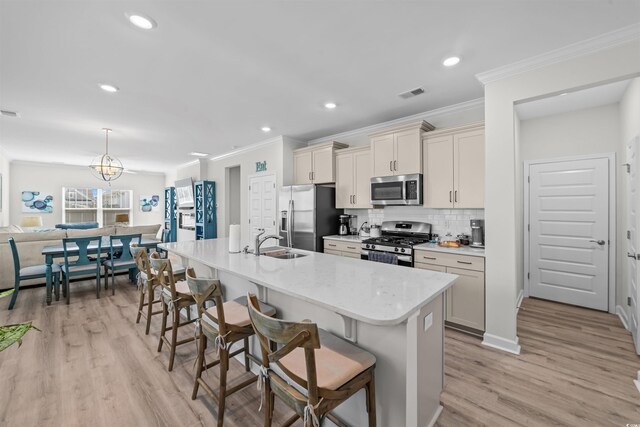 kitchen with a breakfast bar area, appliances with stainless steel finishes, a kitchen island with sink, and light hardwood / wood-style flooring